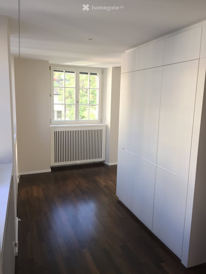 Empty room with wooden floor, white walls, a window, and a white radiator.