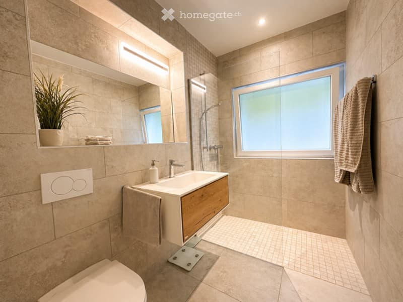 Modern bathroom with beige tiles, a white sink, wooden cabinet, and a glass shower enclosure.