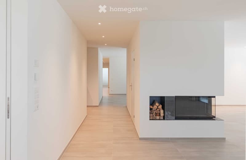 Empty corridor with white walls, wooden floor, and a fireplace with stacked wood.