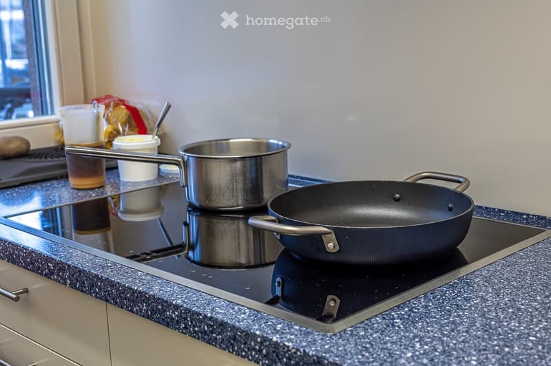 Kitchen with a black induction hob, a frying pan, and a saucepan on it.