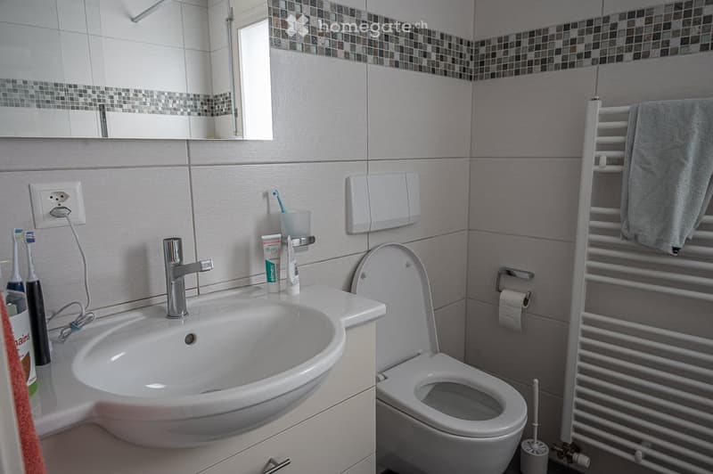 Modern bathroom with white tiles, a sink, toilet, and a towel rack with a towel.