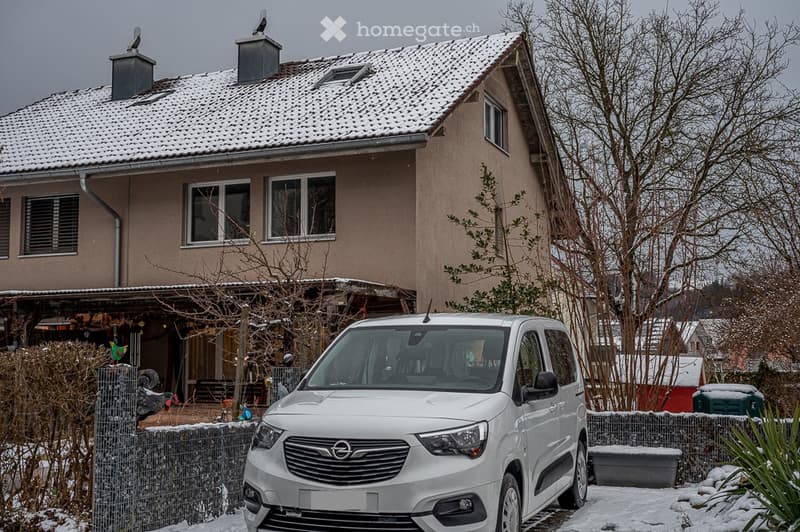 A two-story house with a snow-covered roof, chimneys, and windows. A white van is parked in front of the house.