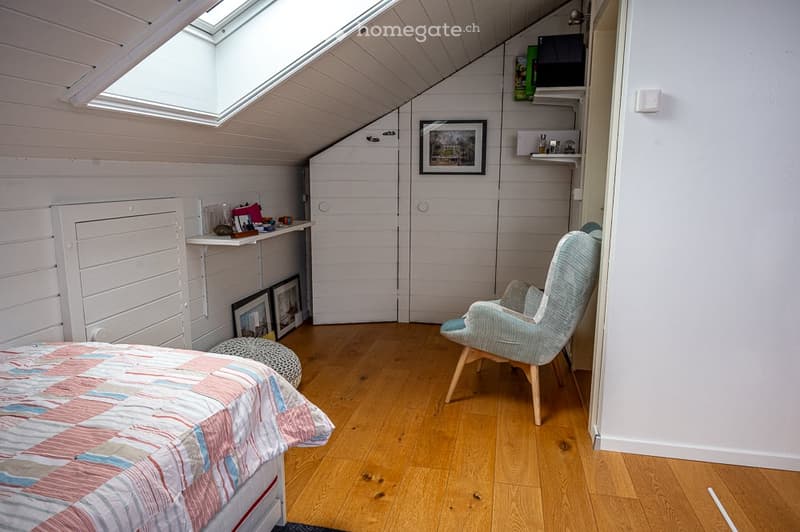 Bedroom with wooden floor, bed, chair, picture frames, shelf, and ottoman.