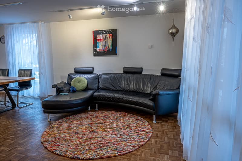 Modern living room with a black leather sofa, round rug, and a painting on the wall.