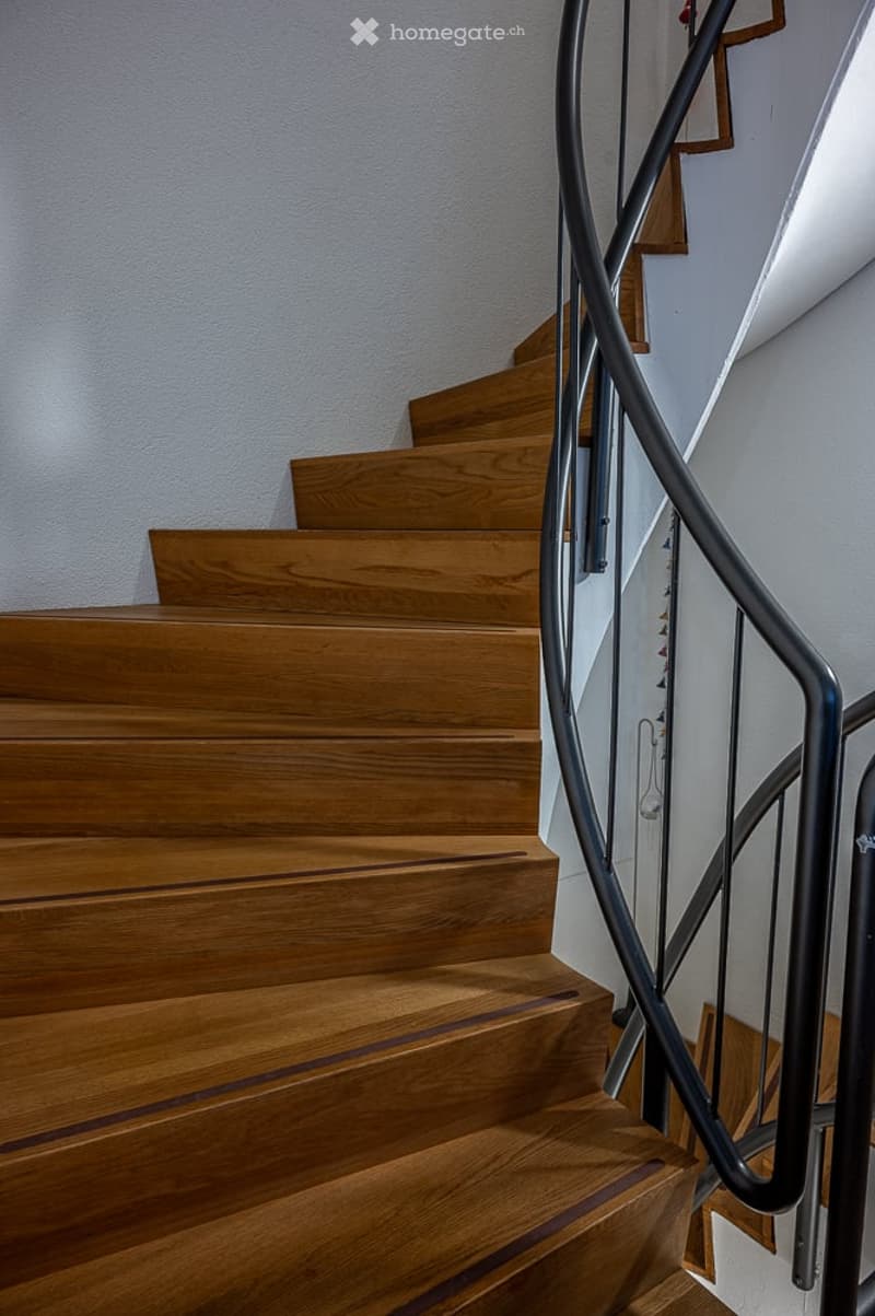 A spiral staircase with wooden steps and a black metal handrail.