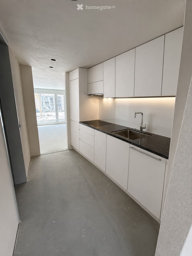 Modern kitchen with white cabinets, black countertops, stainless steel sink, and a faucet.