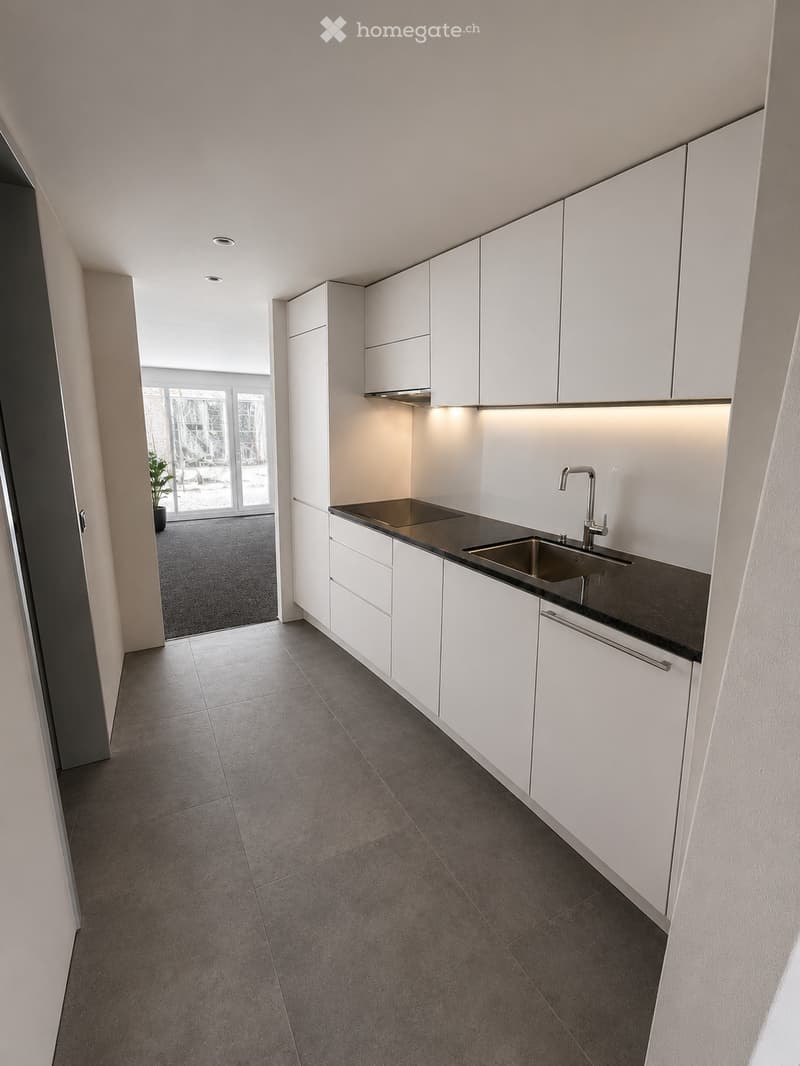 Modern kitchen with white cabinets, dark countertops, and a stainless steel sink. The space features recessed lighting and a tiled floor.
