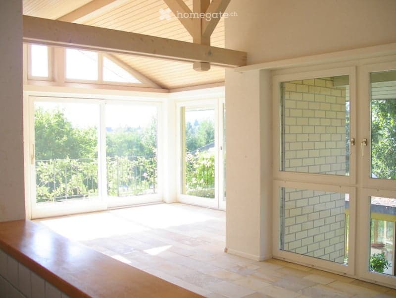 Empty room with wooden ceiling beams, tiled floor, and large glass doors leading to a balcony.