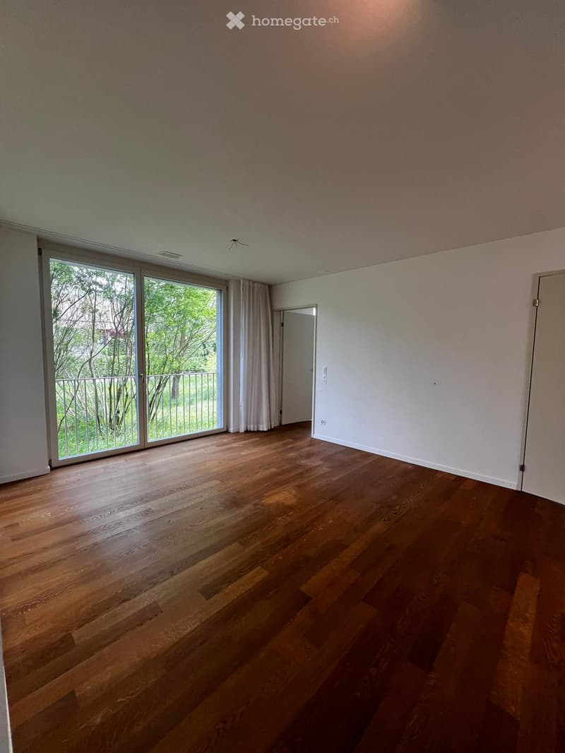 Empty room with hardwood floors, large sliding glass doors leading to a balcony, white walls, and a white door.