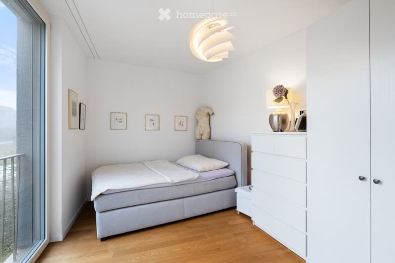 small bedroom with a bed, lamp, small dresser, and cabinet with open doors, balcony, and view to outside