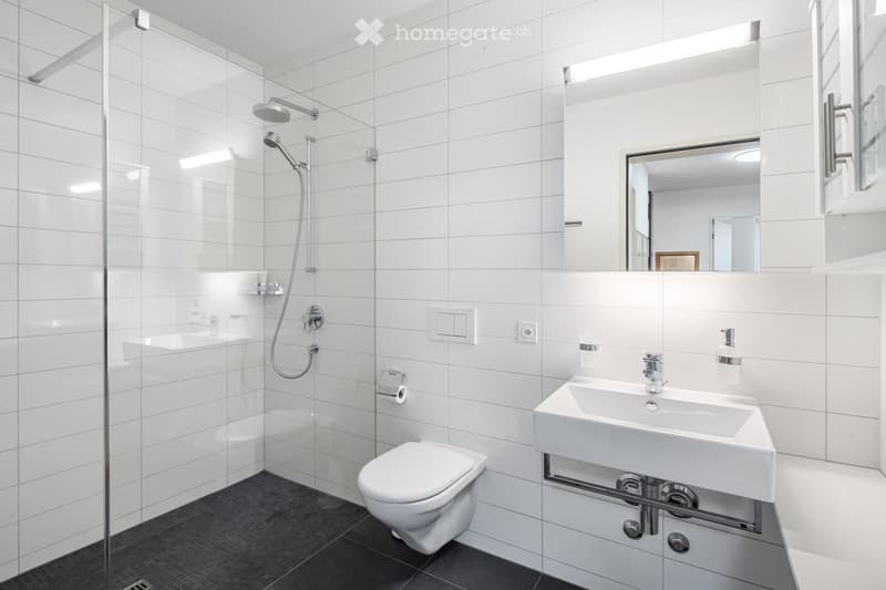 bathroom with white tiles, glass shower enclosure, white toilet, sink, mirrors, and wall-mounted soap dispenser