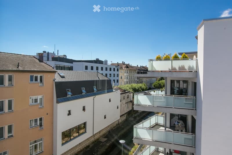 Aerial view of a building with multiple balconies, surrounded by other buildings and greenery.