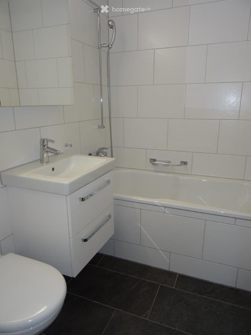 Bathroom with white tiles, white bathtub, white sink, white toilet, silver faucet, silver shower head
