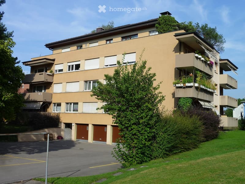 multi-story building, beige exterior, multiple balconies, garage doors, parking lot