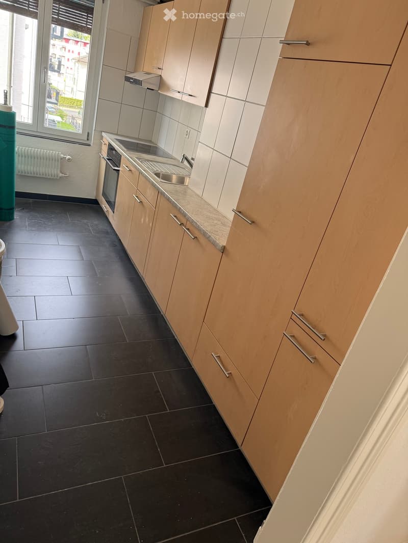 Modern kitchen with wooden cabinets, tiled floor, and a sink with faucet. Oven and a radiator are also present.