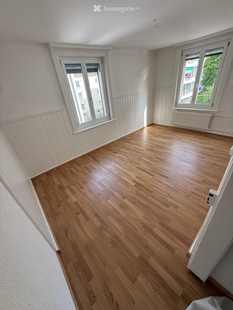 Empty room with wooden floors, white walls, and white-framed windows. No furniture or equipment.