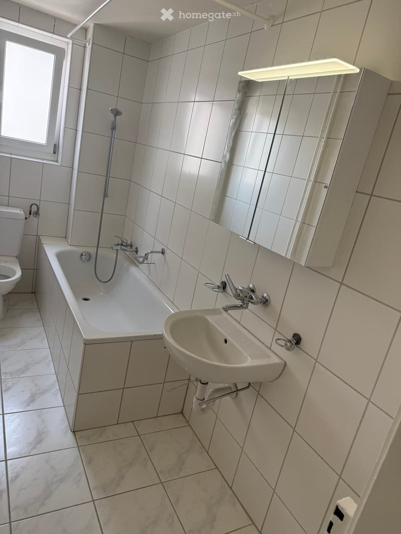 Bathroom with white tiles, bathtub, toilet, sink, and mirror.