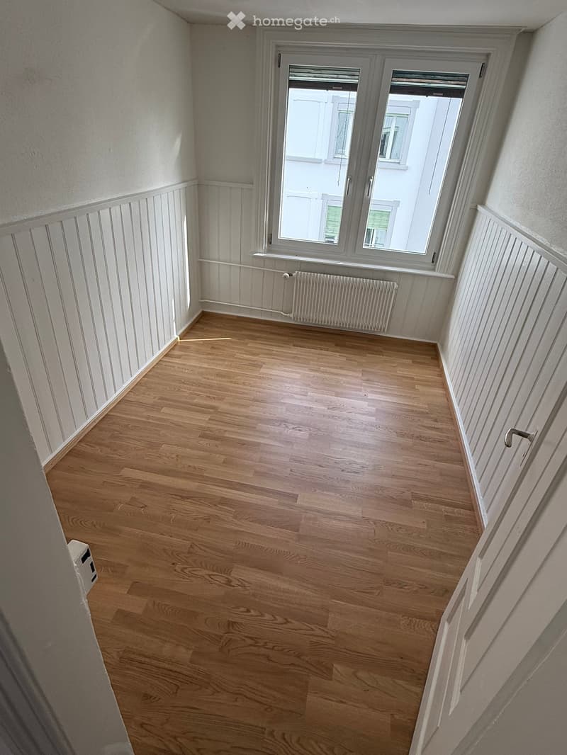 Completely empty room with wooden floor and white walls. There is a window with a white radiator below it.