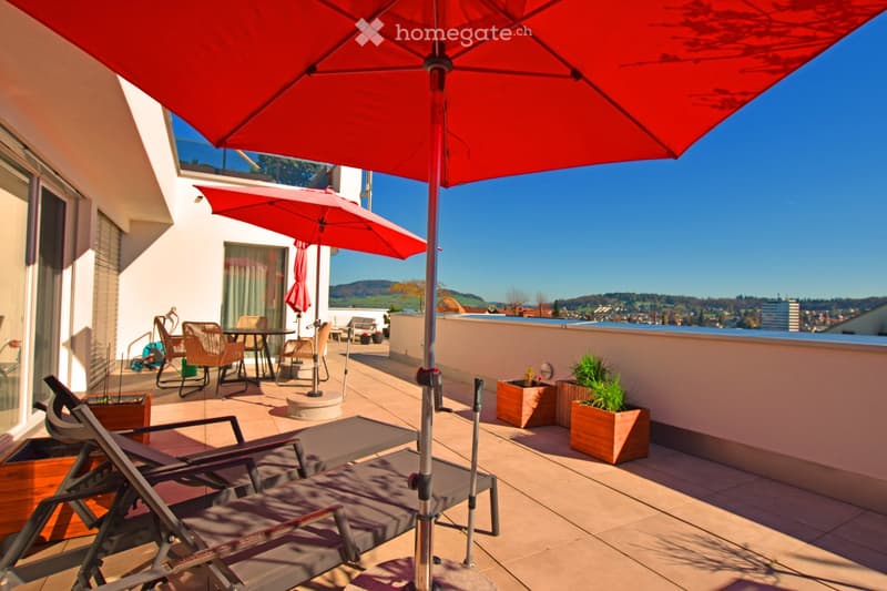 Terrace with lounge chairs, tables, chairs, and umbrellas, with a view of the city