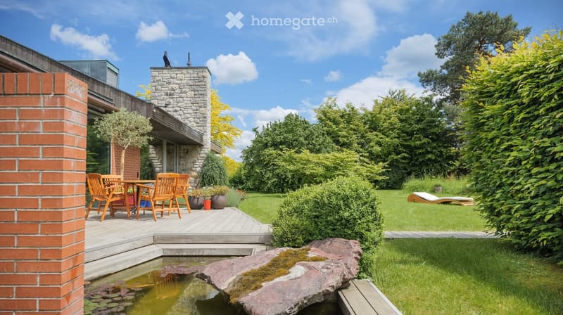 Outdoor dining table, chairs, wooden deck, brick wall, large rock, pond, greenery