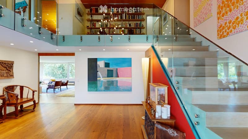 Modern house with wooden floors, raised ground floor, glass staircase, wooden seating, large painting, bookshelves, view to the garden