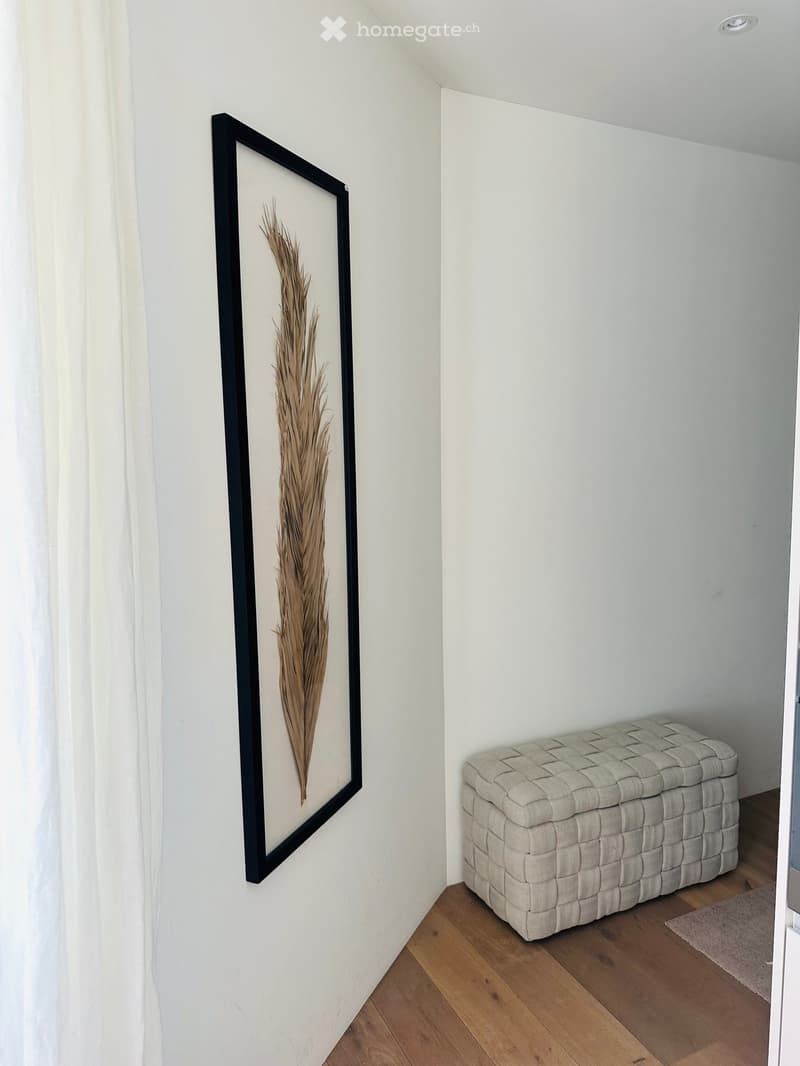 Unfurnished Room. Corner of a room with a white wall, a framed picture, and a woven storage bench.
