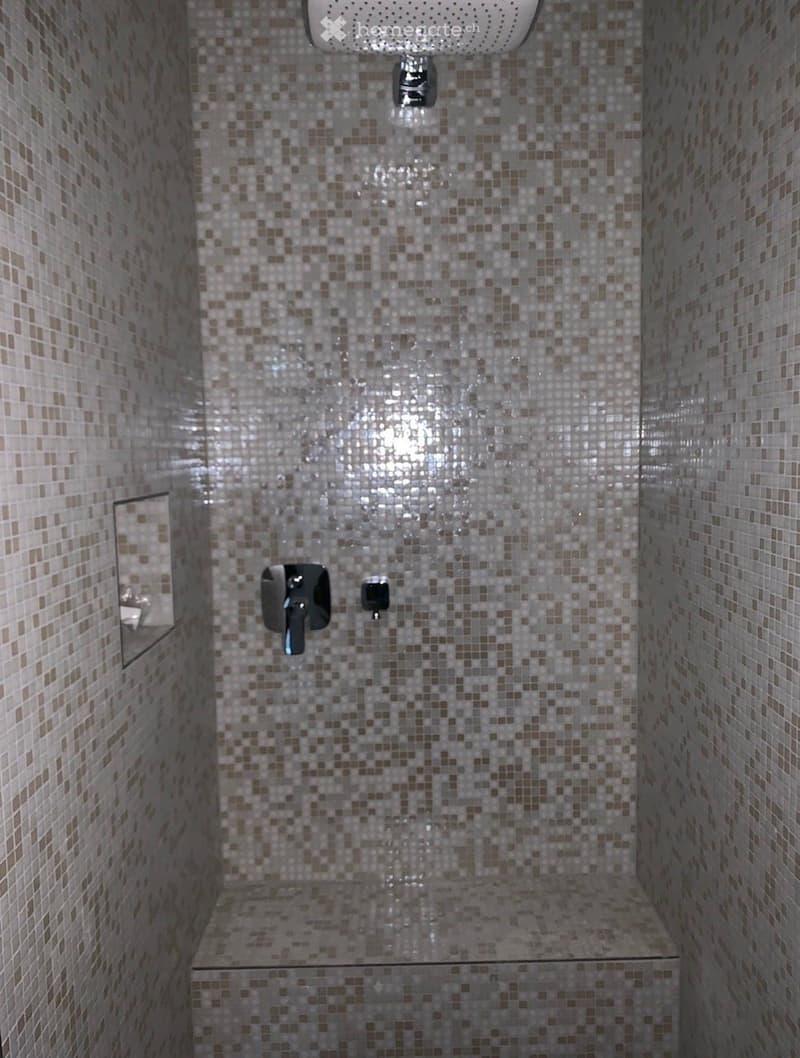 Bathroom. Modern bathroom with tiled walls, shower area, and a bench. The shower head and faucet are silver, and there is a small mirror on the wall.