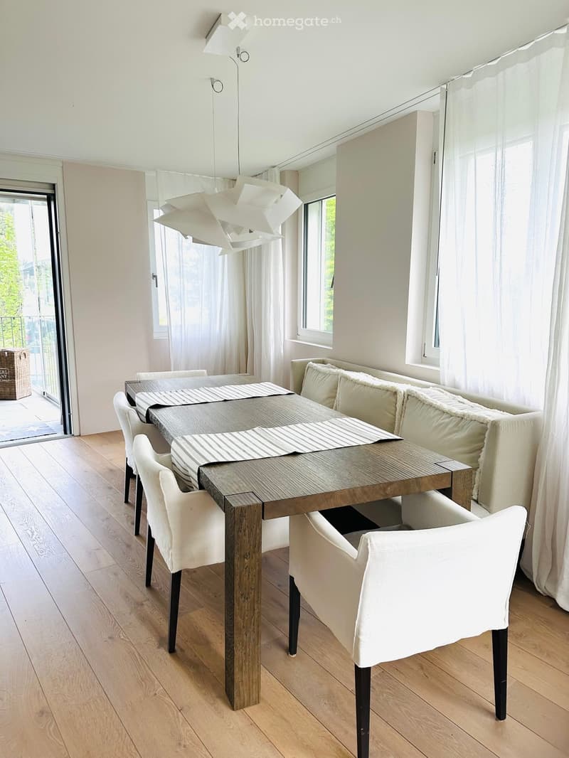 Furnished Room. Dining area with a wooden table, white chairs, and a white bench. The room has white walls, wooden floors, and white curtains.