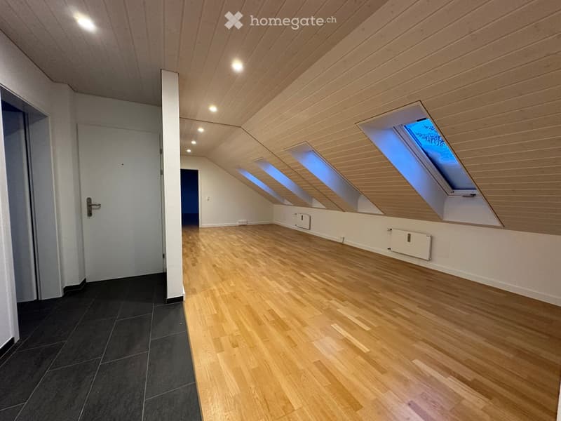 Empty room with wooden floors, white walls, and a ceiling with wooden panels and skylights.
