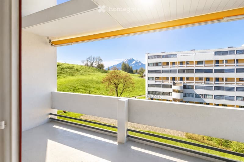 Balcony with railings, view of a grassy hill and a building, white walls, white ceiling