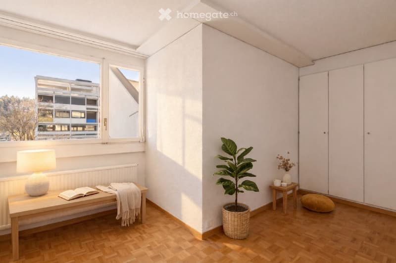 Empty room with wooden floor, white walls, large window, bench, lamp, potted plant, small table, and a white radiator.
