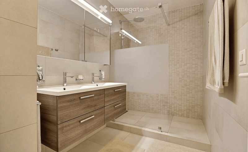 Modern bathroom with a double sink, wooden cabinet, and a glass shower enclosure.