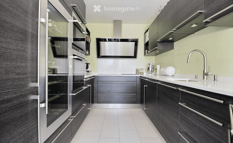 Modern kitchen with dark cabinets, white countertops, stainless steel appliances, and a sleek design.