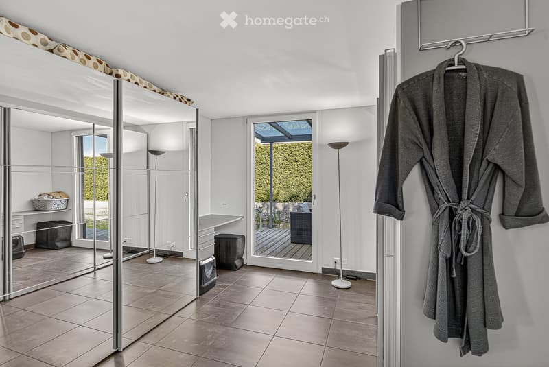 Spacious room with tiled floor, large mirror, robe hanging on a hook, and a desk with a basket on top.
