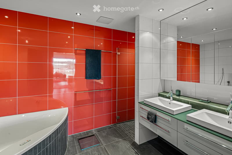 Modern bathroom with red tiles, white bathtub, double sinks, and a large mirror.