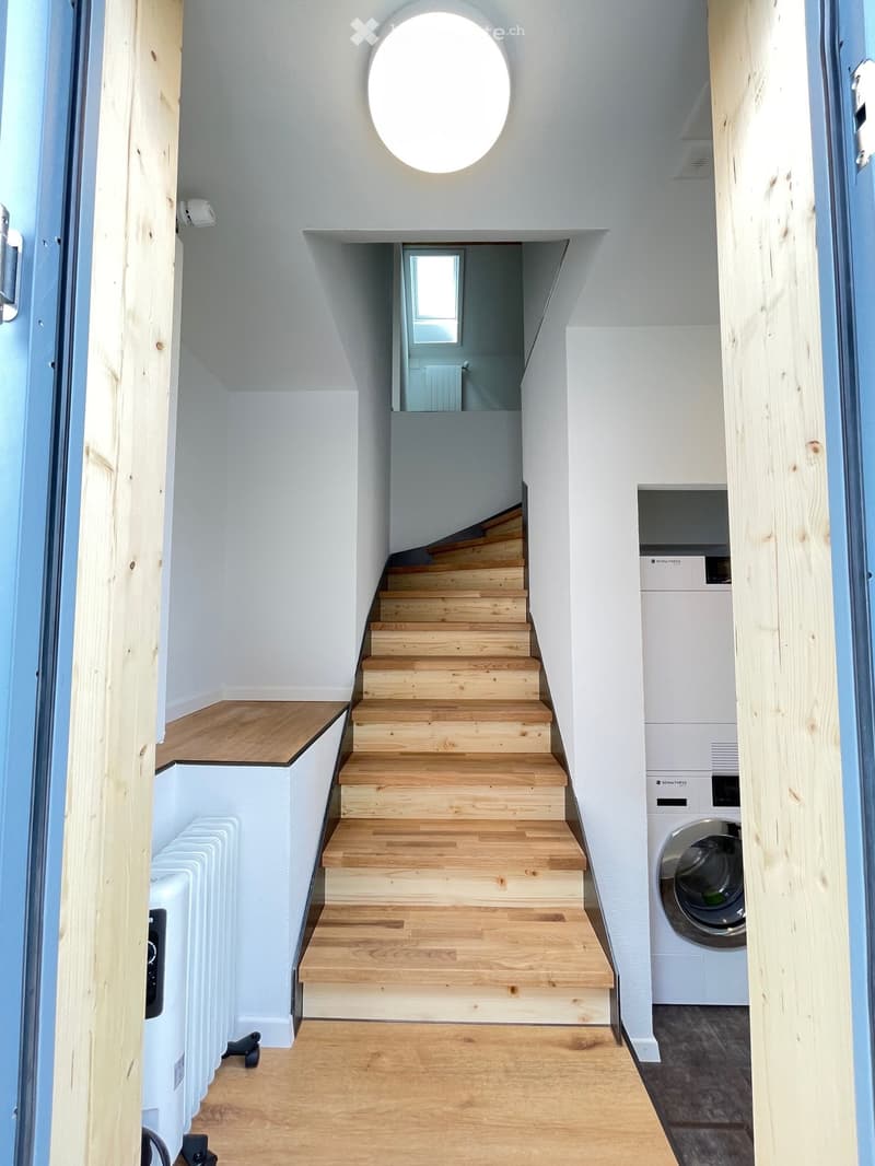A corridor with wooden stairs, a ceiling light, a radiator, and a washing machine.