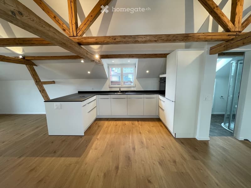 Modern kitchen with wooden beams, white cabinets, black countertops, and a sink with a faucet.