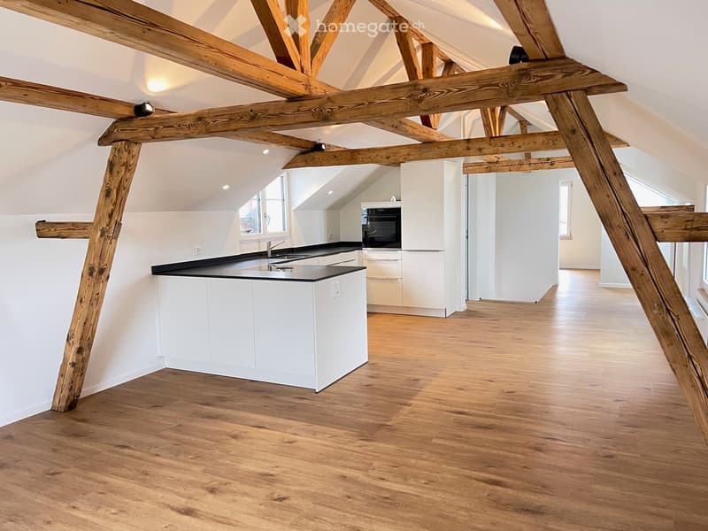 Open kitchen with wooden beams, white cabinets, black countertops, and a modern kitchen island.