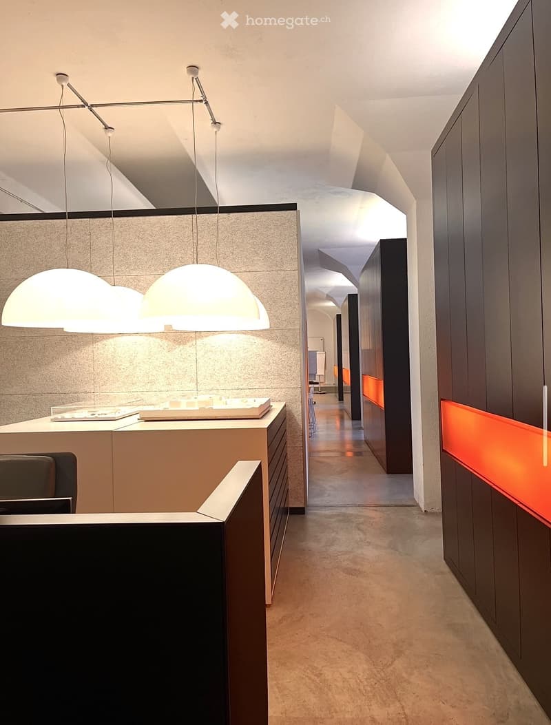 modern office room with white walls, gray ceiling, three hanging lamps, a desk, a chair, and a cabinet with drawers