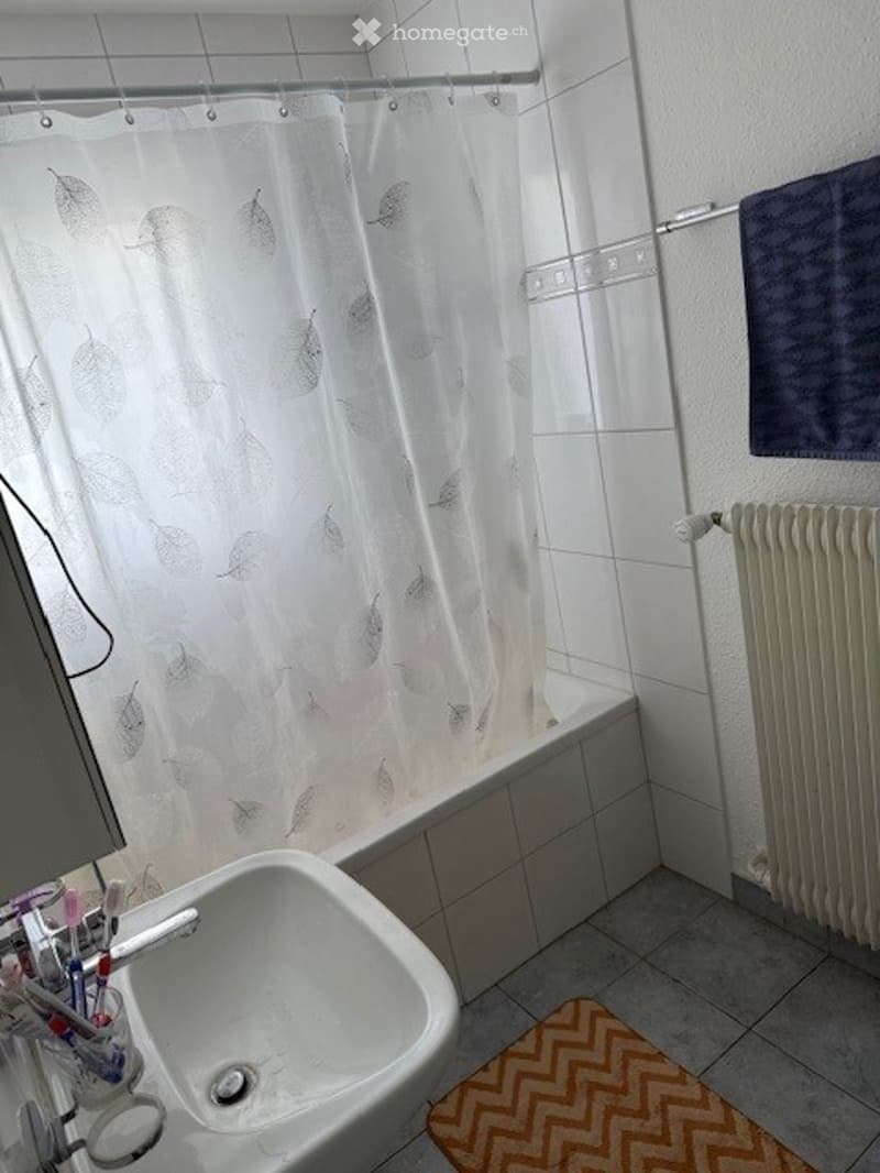 Bathroom with white tiles, a bathtub, a sink, a shower curtain, a towel, and a radiator.