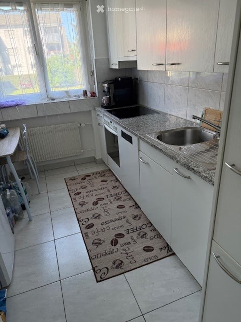 A kitchen with white cabinets, a granite countertop, a sink, and a coffee maker on the counter.