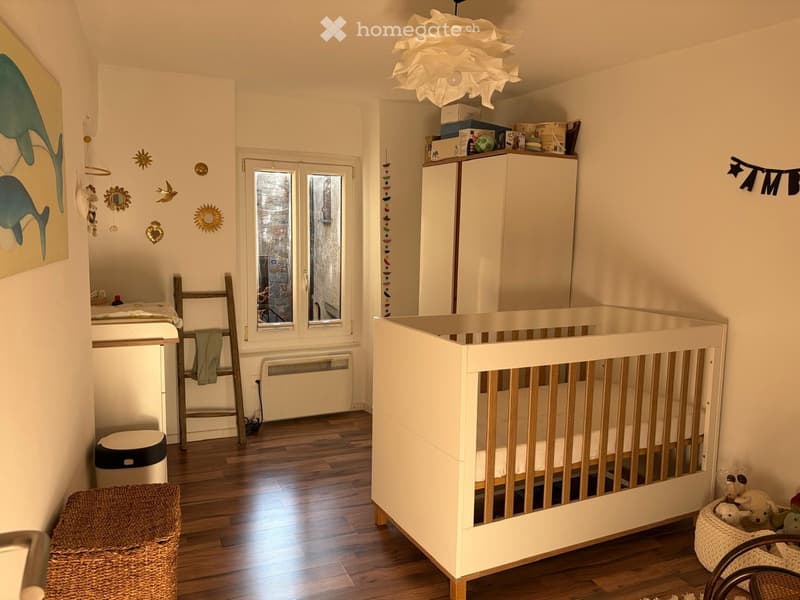 A nursery with a crib, wooden floor, white walls, and various decorative items.