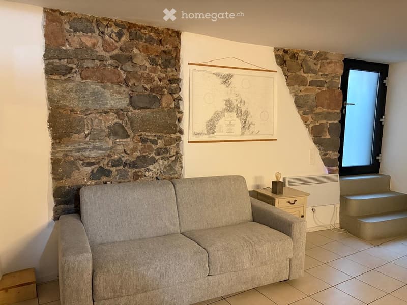 A living room with a gray couch, a wooden side table, a map on the wall, and a stone wall.