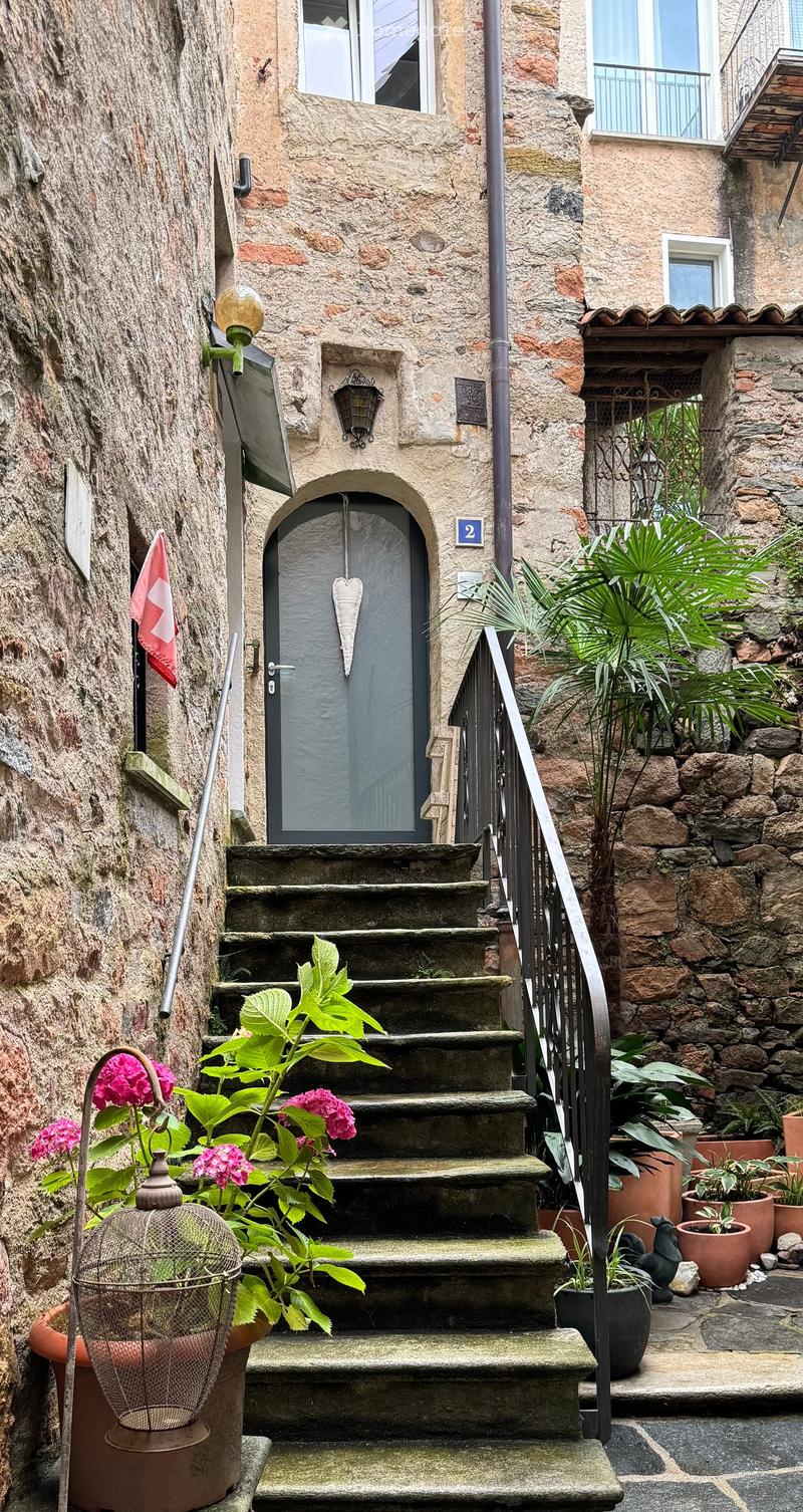Stone wall, concrete steps, metal railing, door, plants, flag