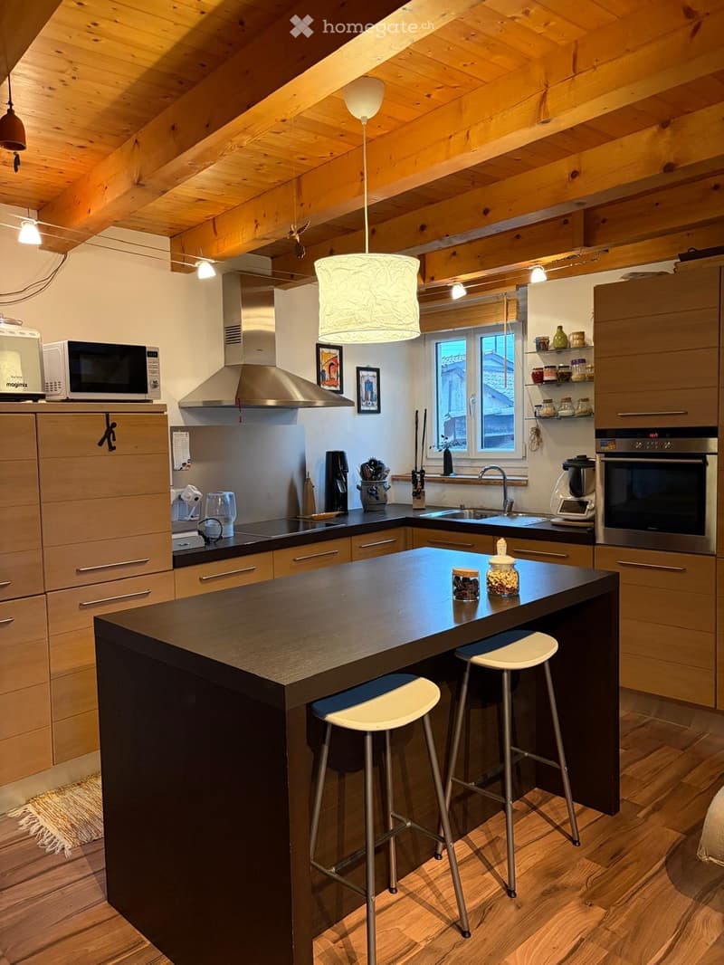 modern kitchen with island, wooden cabinets, black countertops, two stools, hanging lamps, microwave, coffee maker, oven, sink, wooden floor
