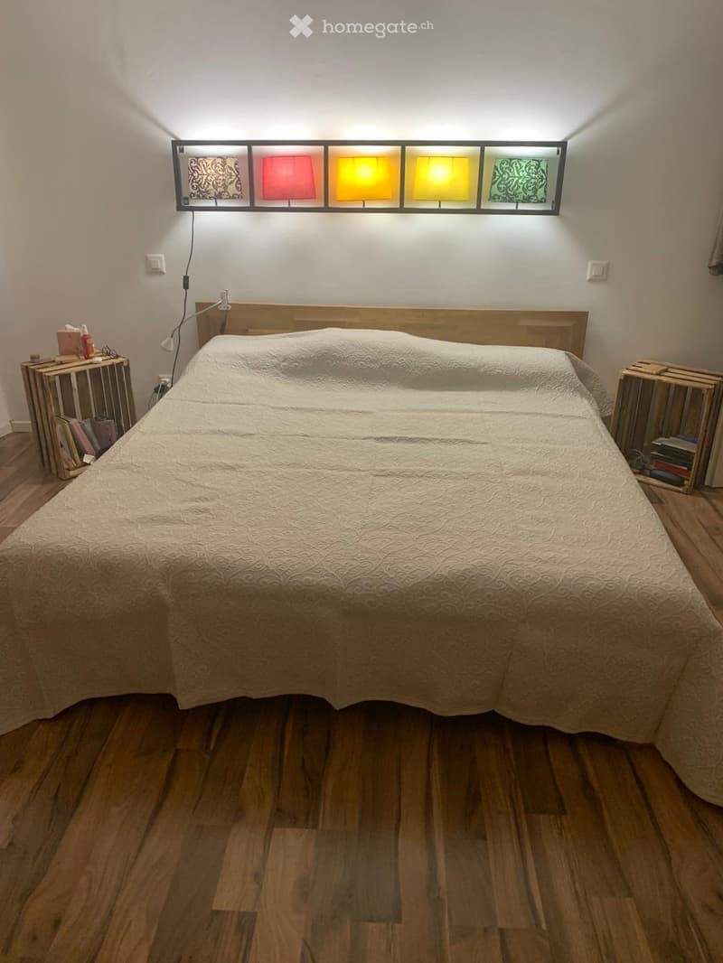 Bedroom with wooden bed, wooden floor, wall-mounted lamp, bedside tables, and a colorful wall lamp.