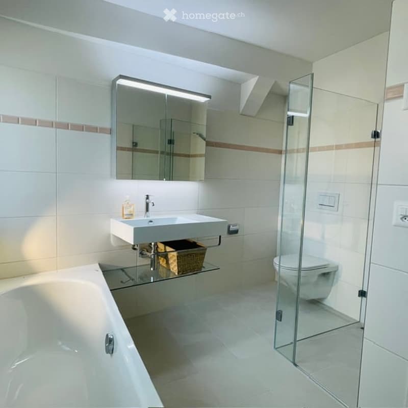 Modern bathroom with white tiles, bathtub, sink, mirror, and glass shower enclosure.