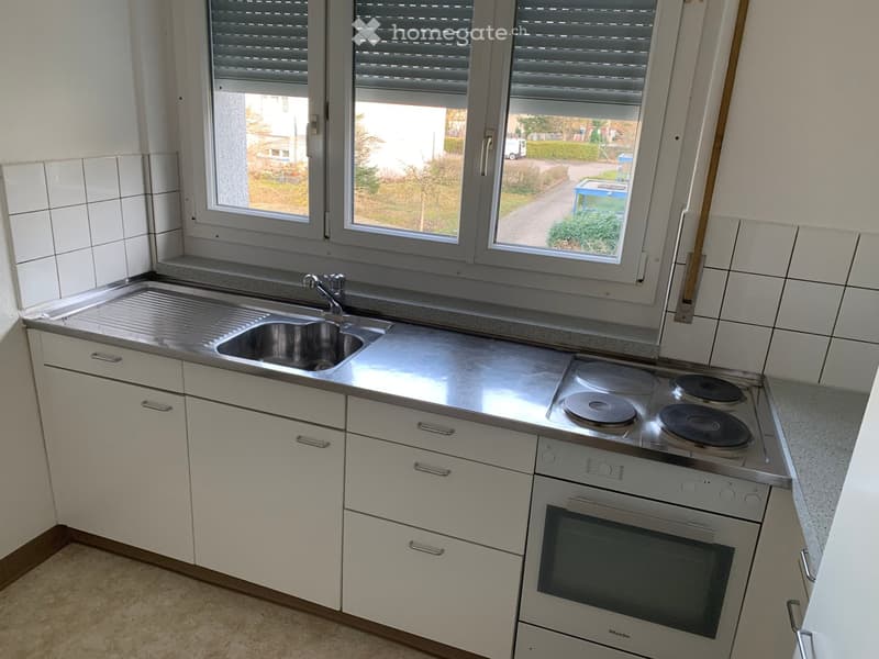 Modern kitchen with white cabinets, stainless steel countertop, sink, stove, and oven.