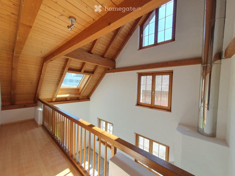 A wooden ceiling with beams, white walls, wooden railings, and windows with wooden frames.