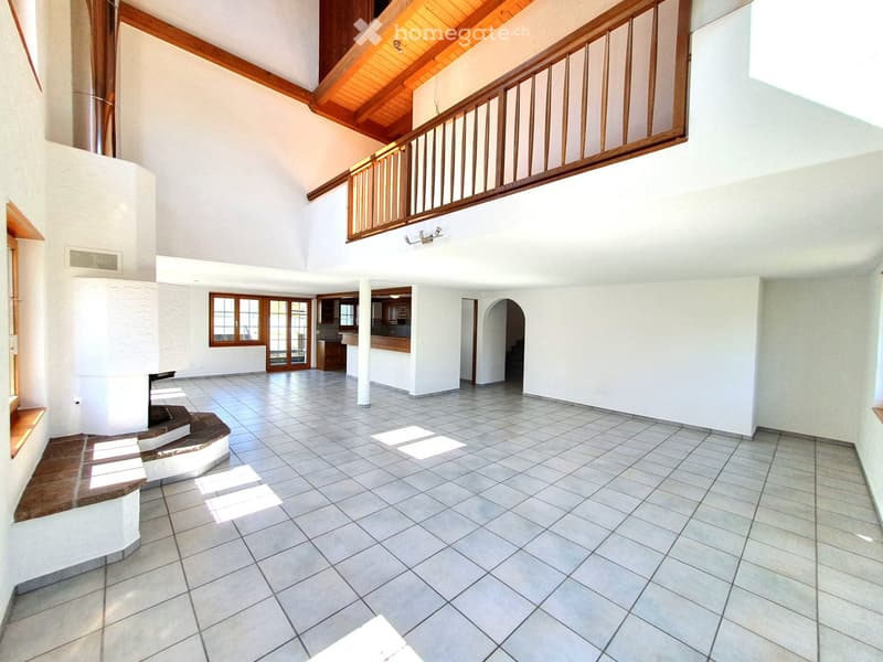 Empty room with white tiled floor, wooden ceiling, and white walls. There is a fireplace and a balcony with a wooden railing.